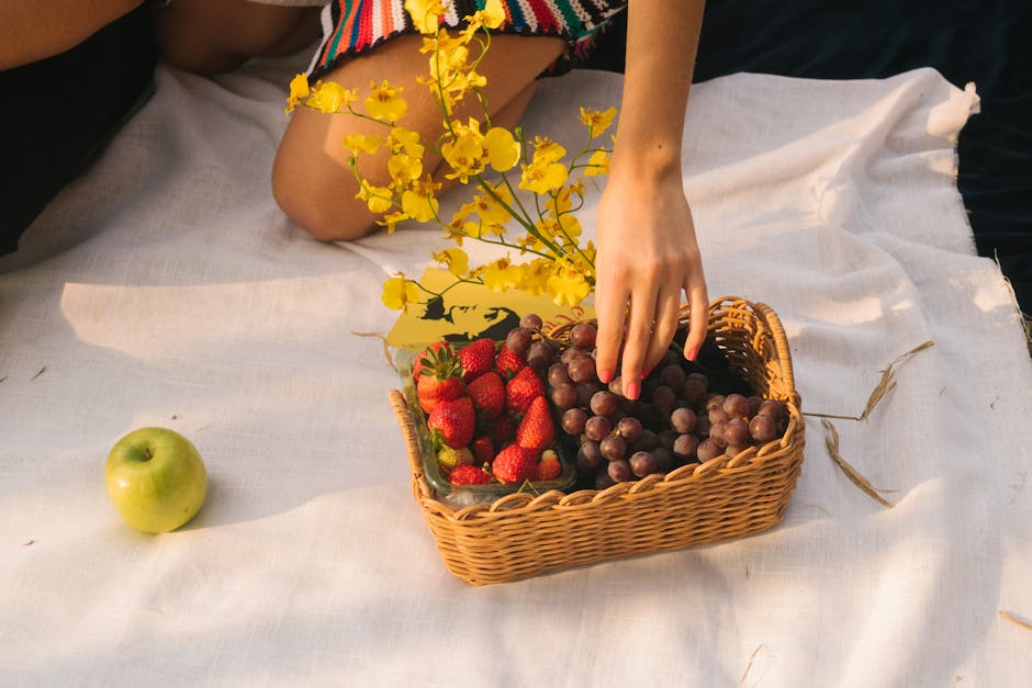 A vibrant picnic setup with strawberries, grapes, an apple, and yellow flowers in a wicker basket.